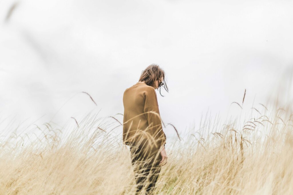 Lost, sad looking person, standing in long grass and looking away.